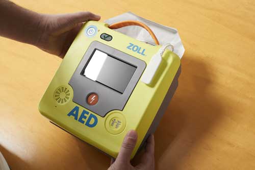 Person holding ZOLL AED 3 over wooden table top.